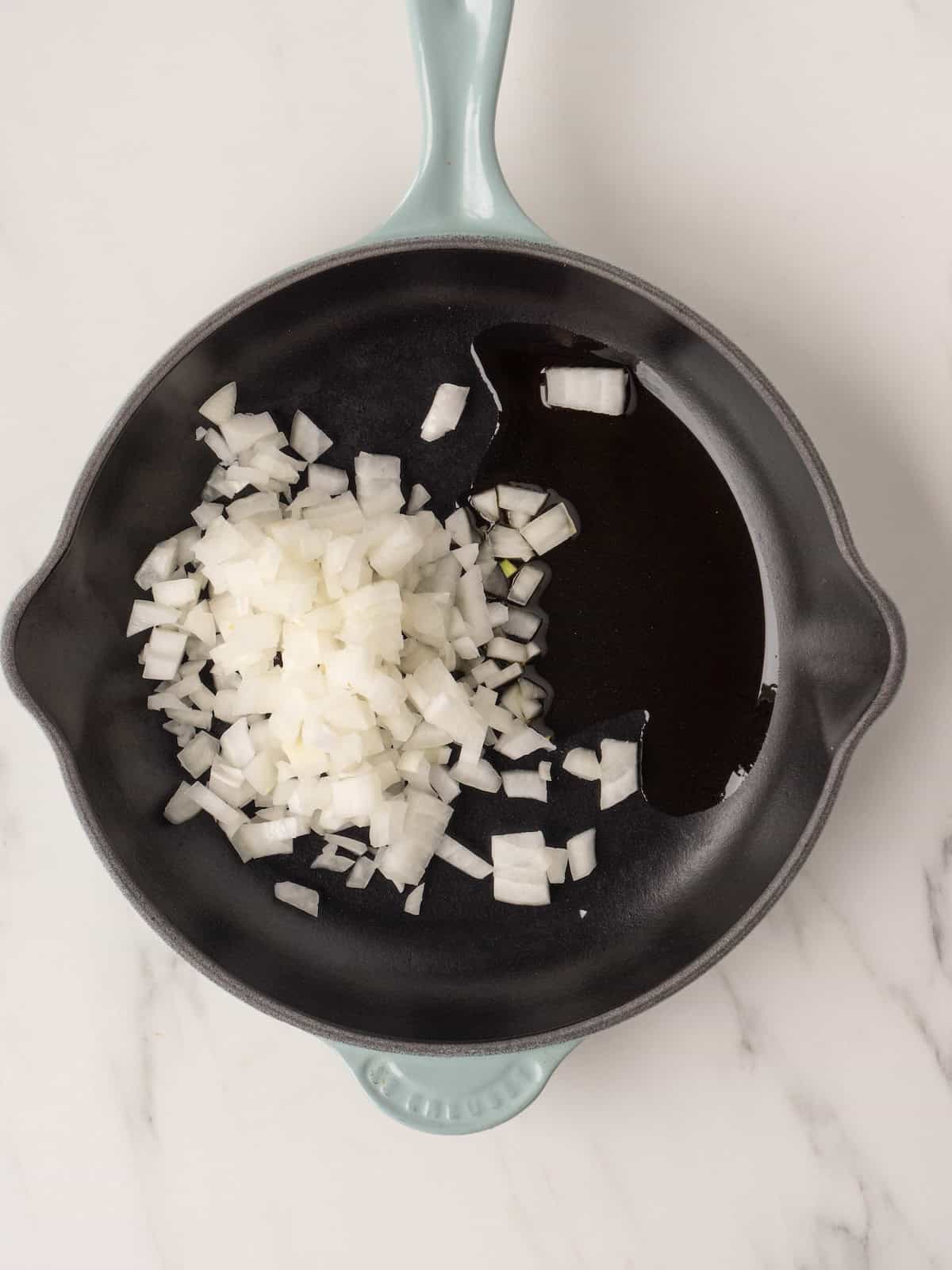 A medium pan with diced onions being sautéed in olive oil.