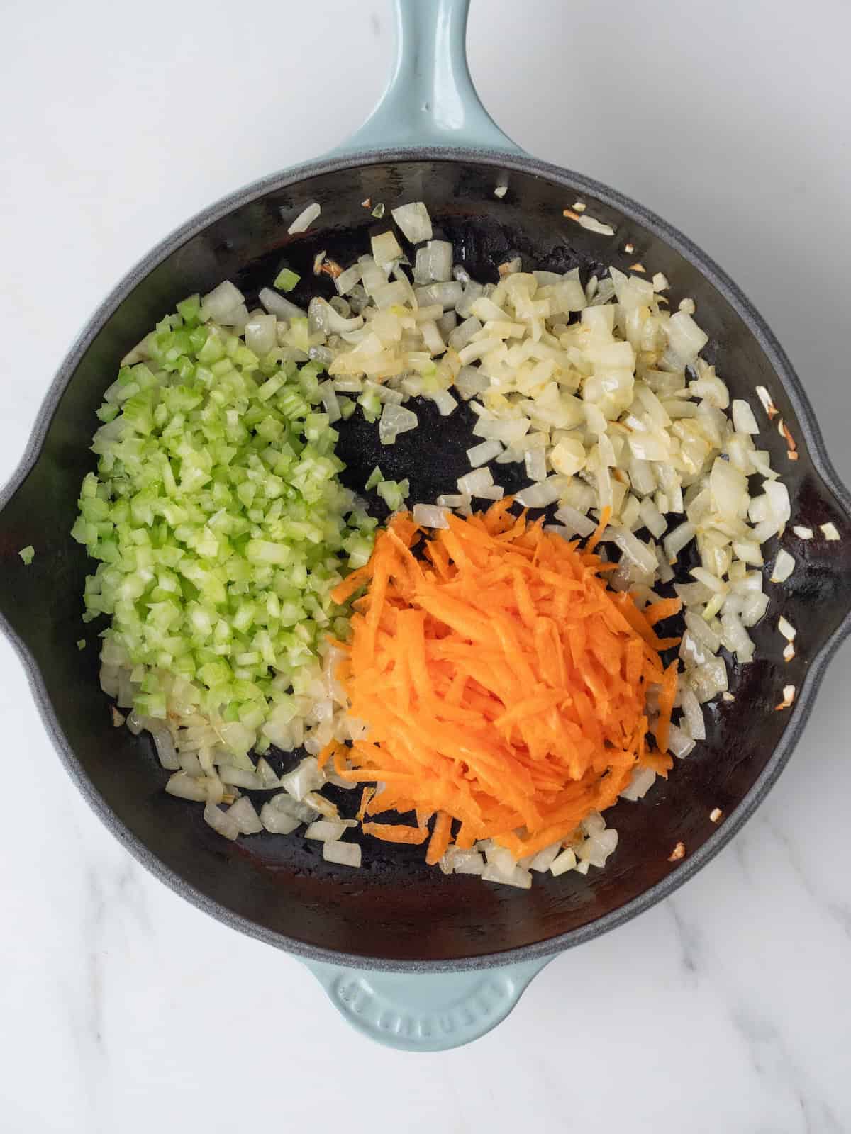 A medium pan with sautéed onions, with grated carrots and diced celery just added.