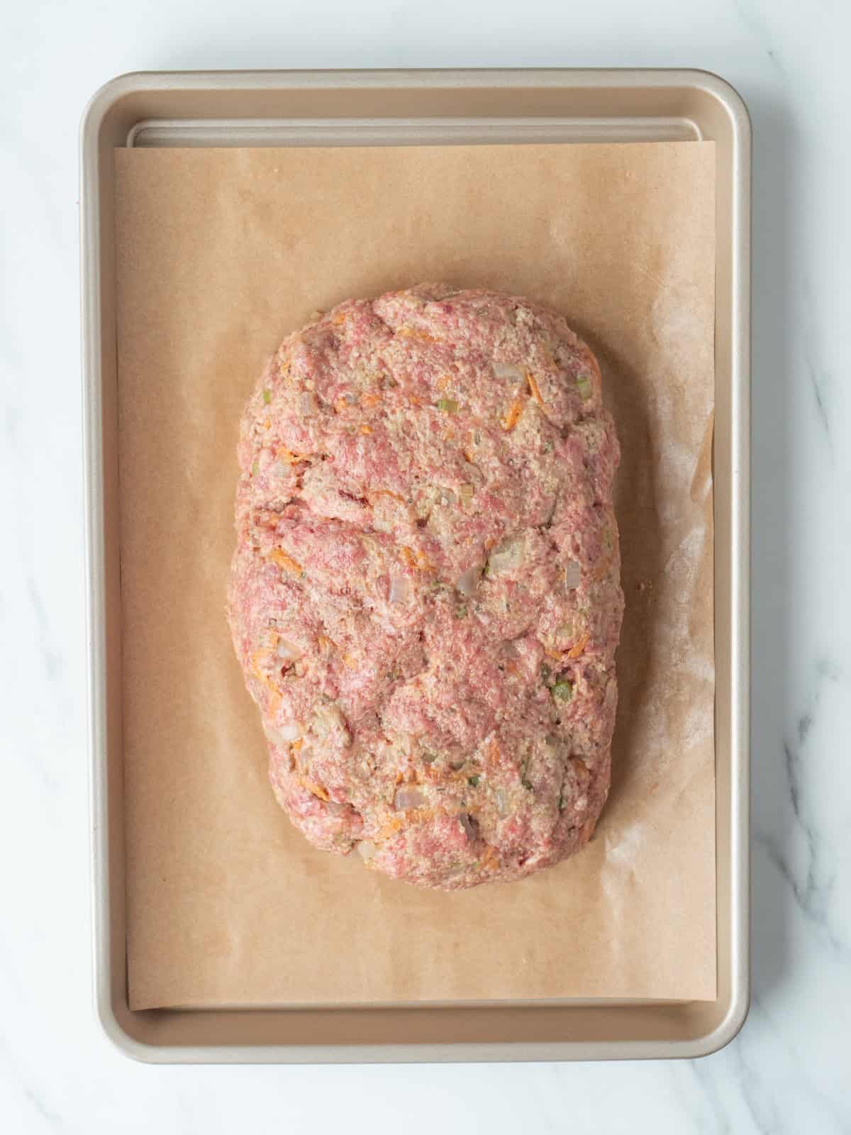 A parchment paper-lined baking sheet with meatloaf mixture shaped into a loaf on it.