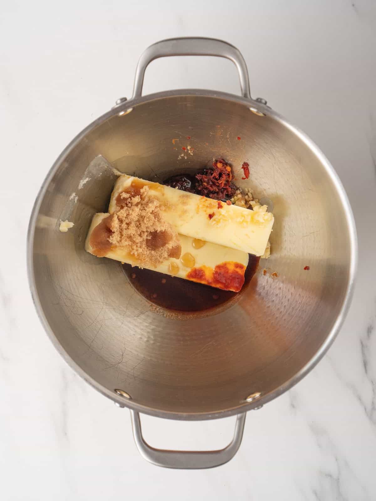 A mixing bowl with two sticks of butter, maple syrup, brown sugar, chipotles in adobo and garlic.