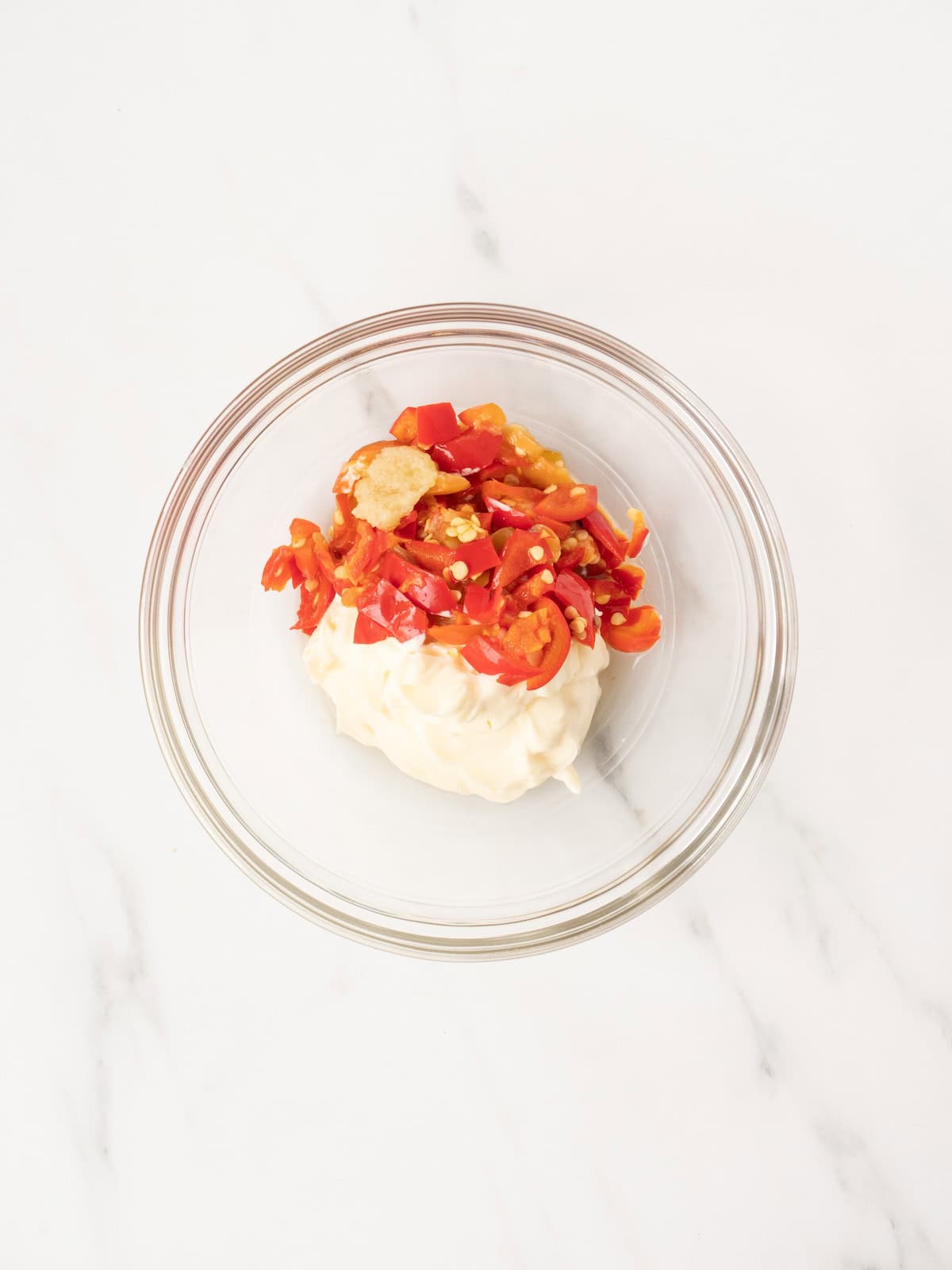 A small mixing bowl with mayonnaise and cut up cherry peppers.