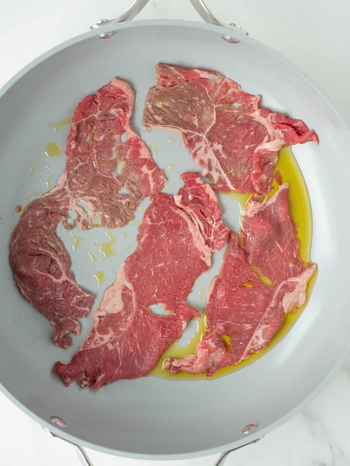 A skillet with some oil and thinly sliced steak being cooked in small batches in a single layer to avoid steaming.