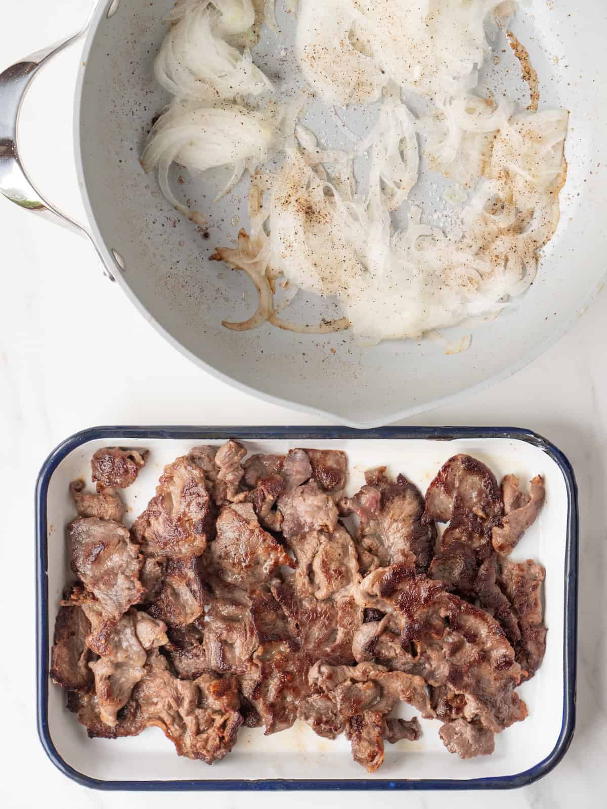 A rectangular dish with cooked steak, along with onions being cooked in the skillet.