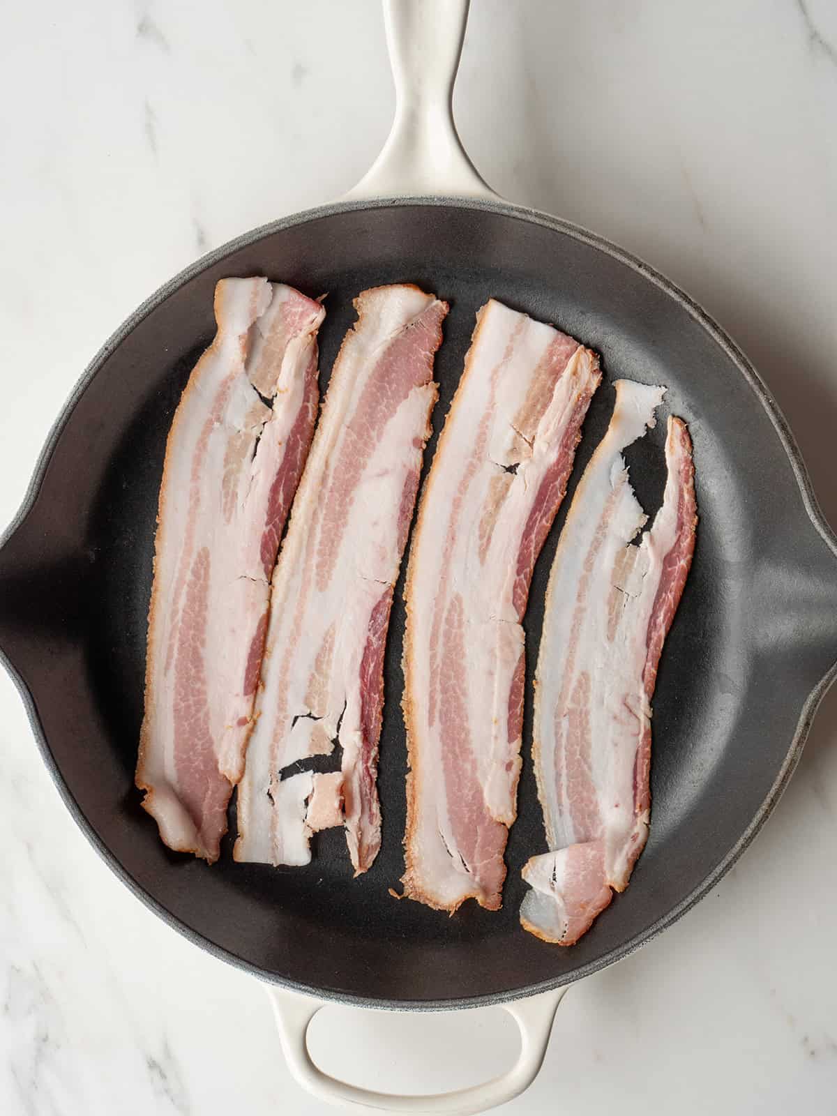 Raw bacon strips in skillet