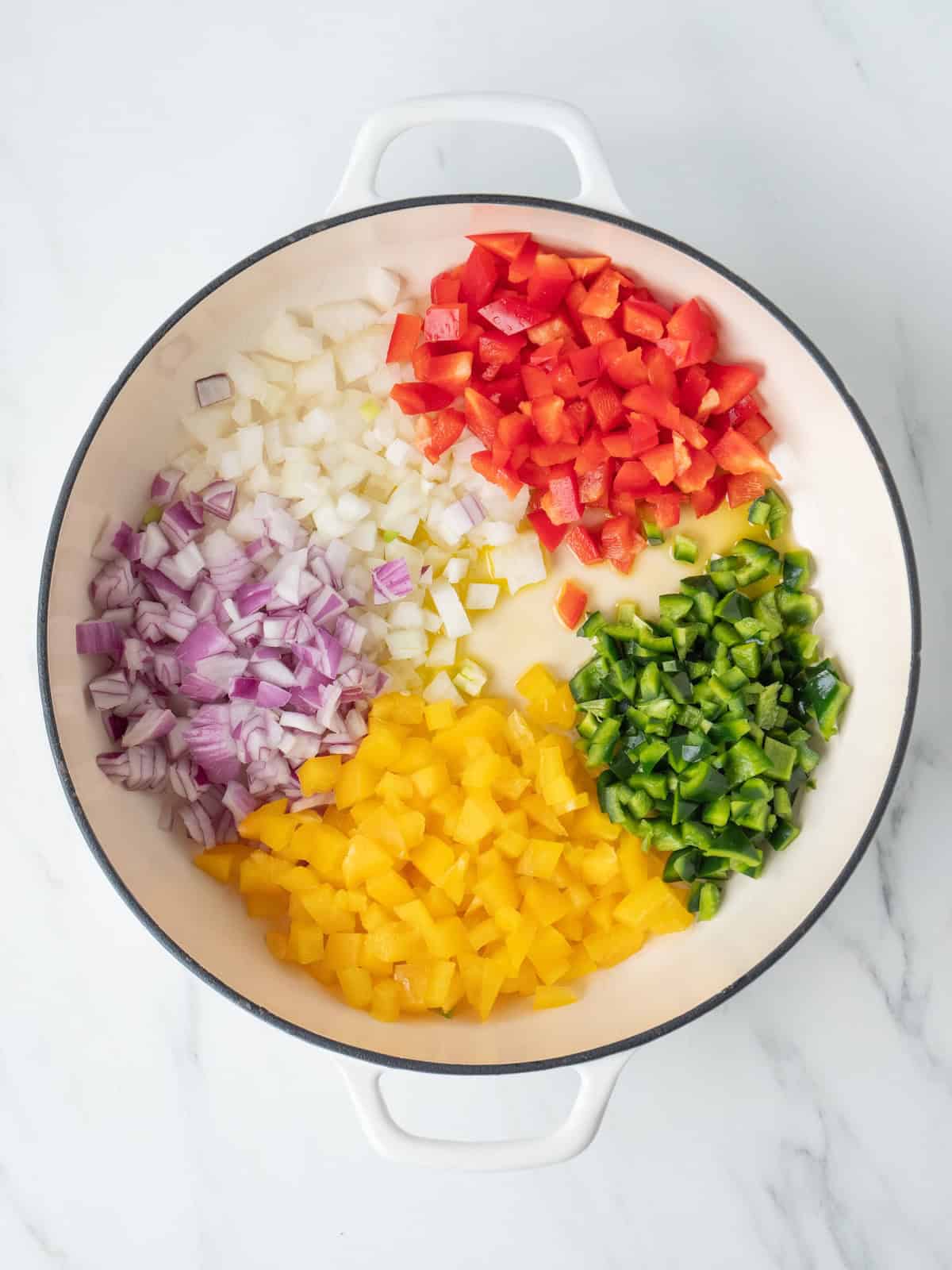 A dutch oven with diced yellow and red bell peppers, yellow and red onions, and poblano pepper being sautéed.