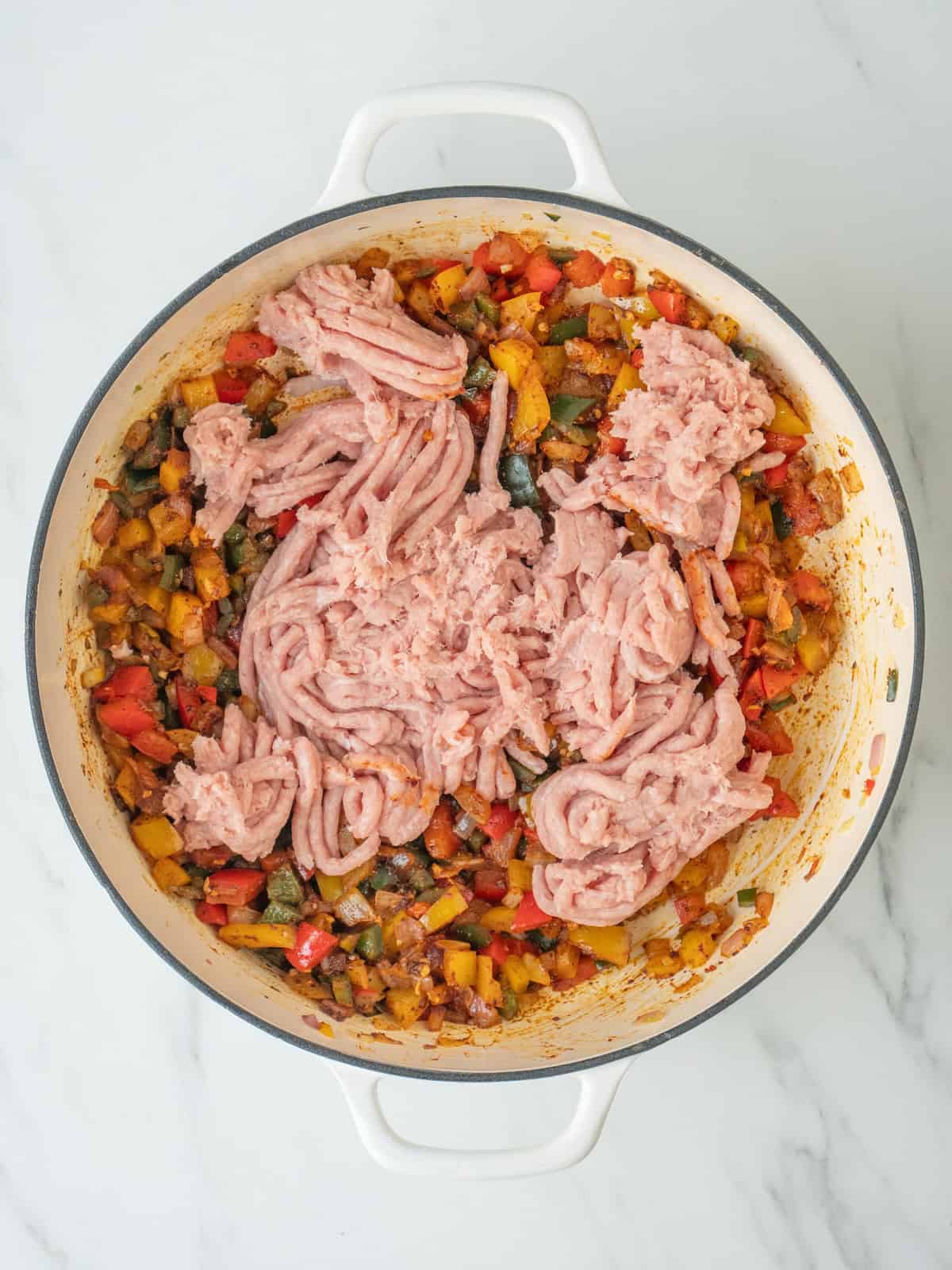 A dutch oven with sautéed bell peppers, onions and poblano pepper and ground turkey just added.