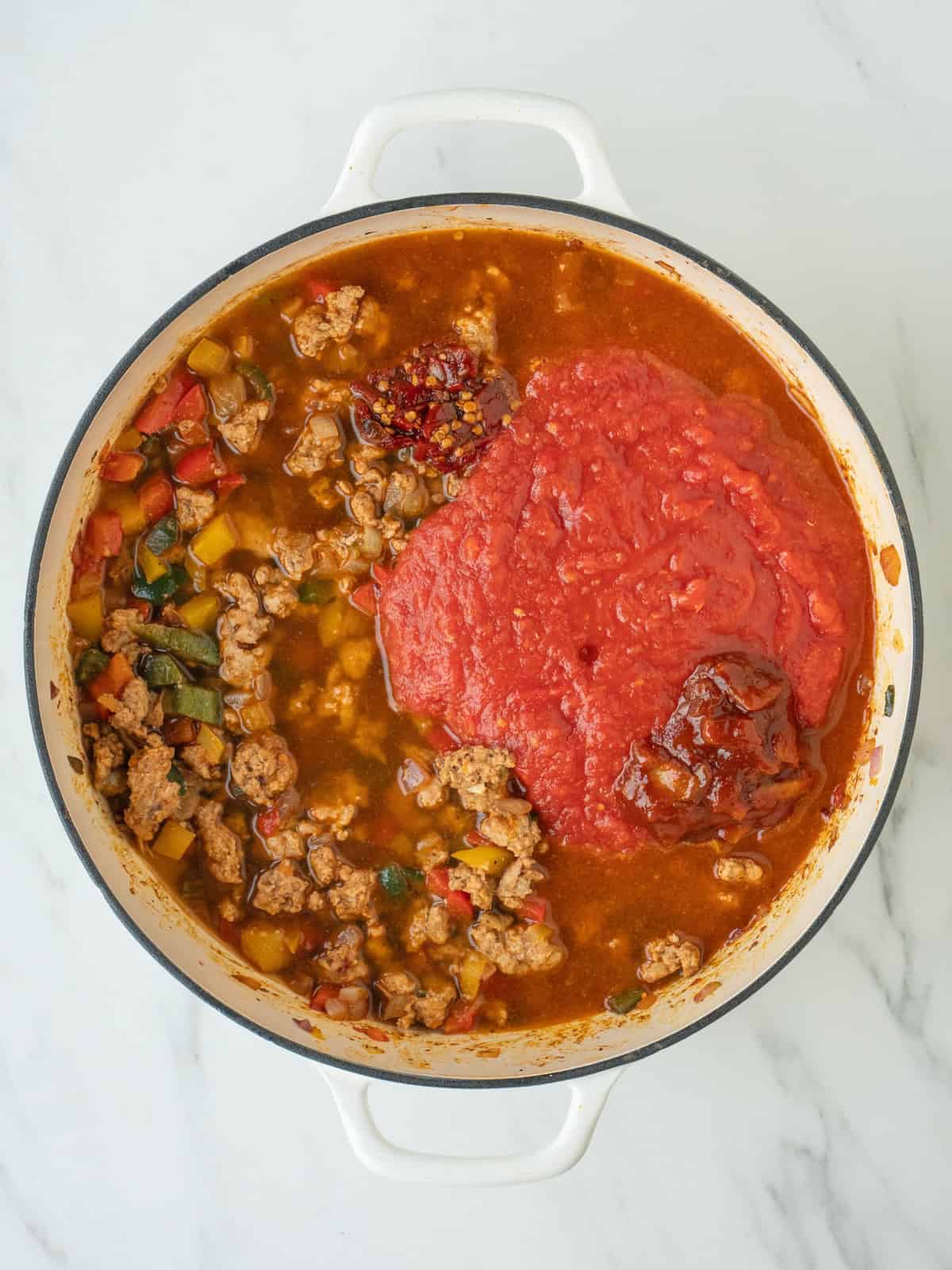 A dutch oven with turkey chili being cooked, with crushed tomatoes, chipotle peppers and adobo sauce just added to it.