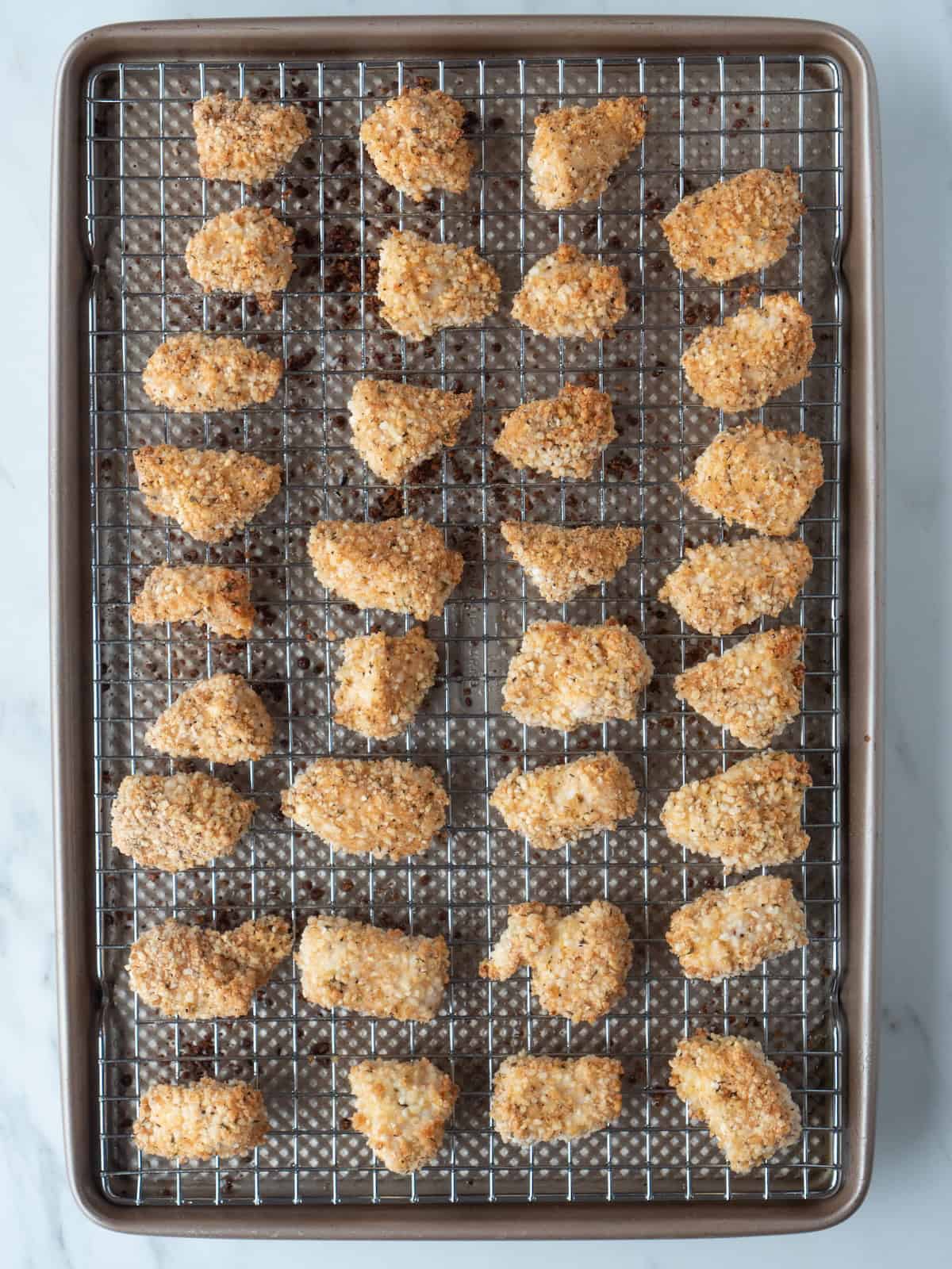 A baking sheet with a wire rack on it with freshly baked homemade chicken nuggets on it.