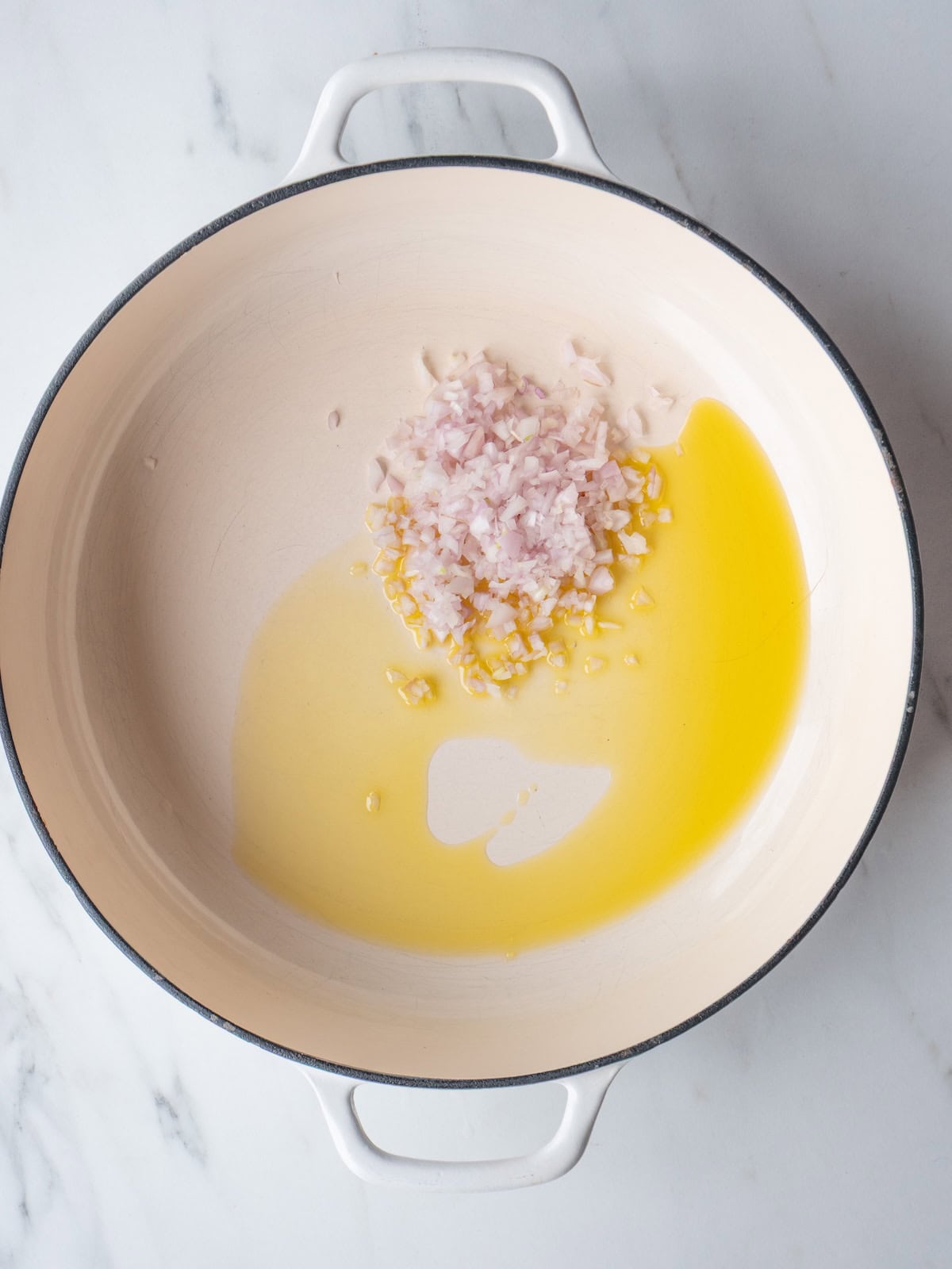 A dutch oven with olive oil and diced shallots being sautéed.