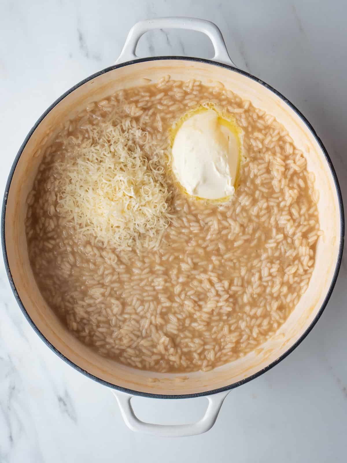 A dutch oven with risotto being cooked, with chicken stock, mascarpone and grated parmesan just added.