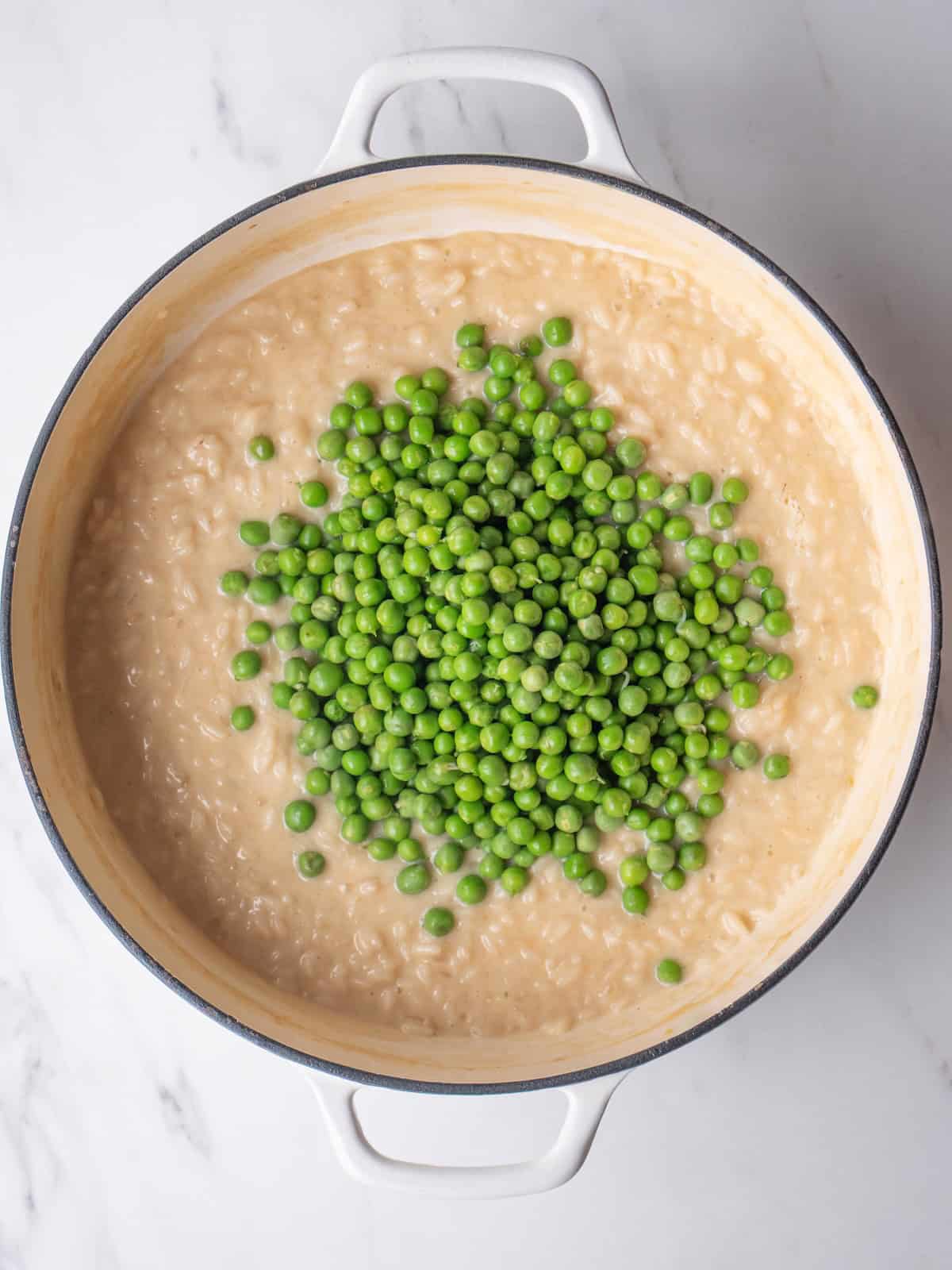 A dutch oven with risotto being cooked, and blanched peas just added.