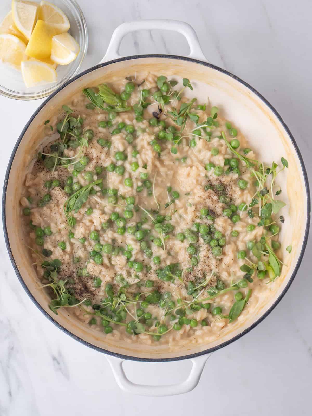 A dutch oven with spring pea risotto garnished with pea tendrils.
