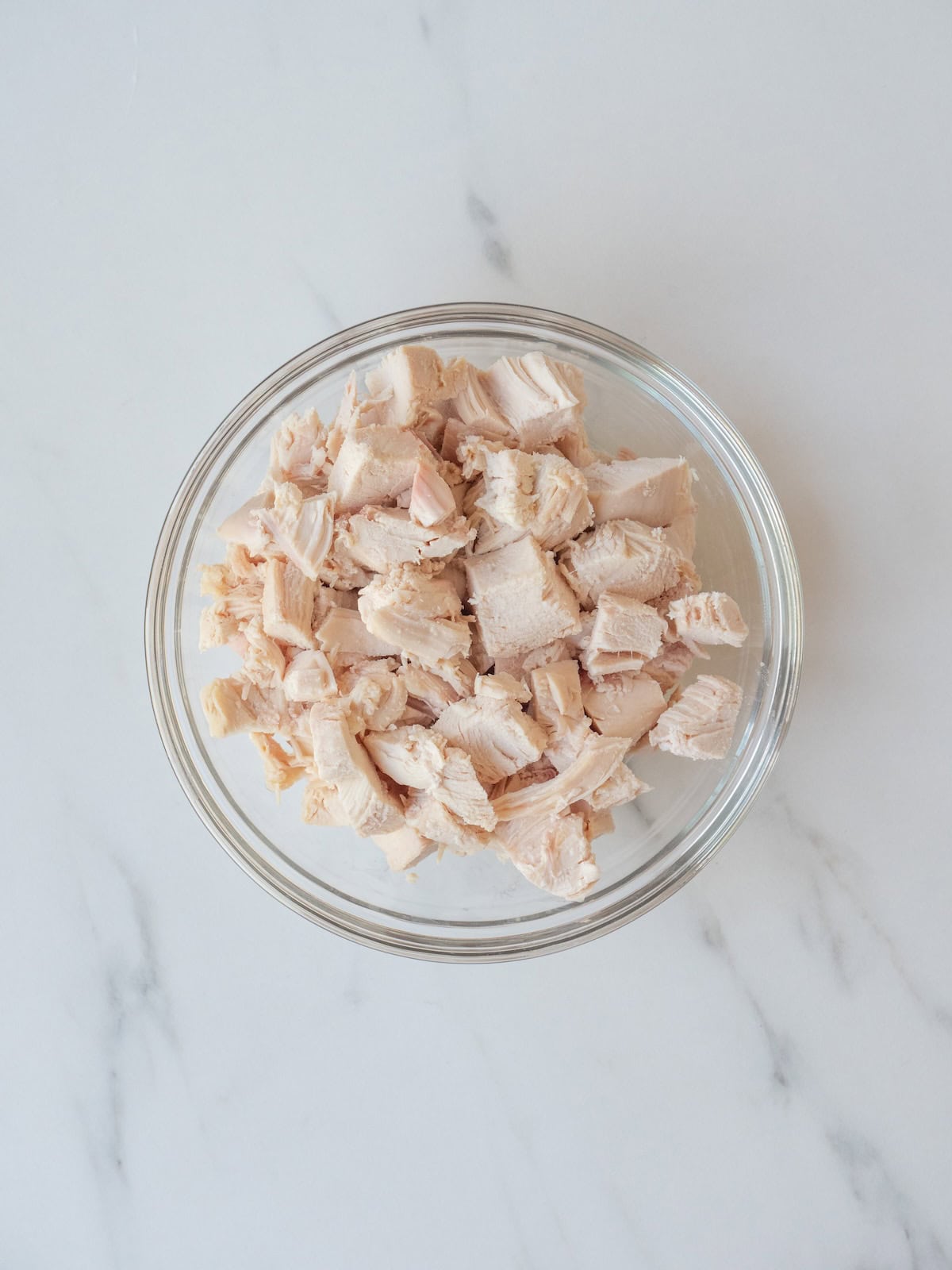 A mixing bowl cooked chicken breast chopped up into half inch cubes.