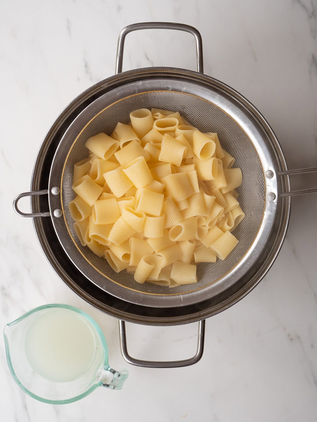 Cooked pasta draining in large pot with pasta water on the side