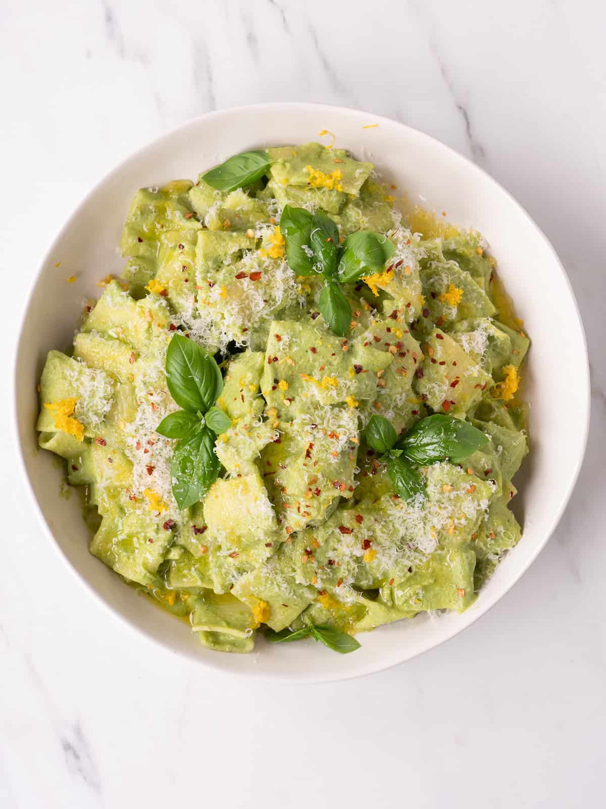 Plated zucchini pasta topped with basil, parmesan, lemon zest, red pepper flakes, and olive oil