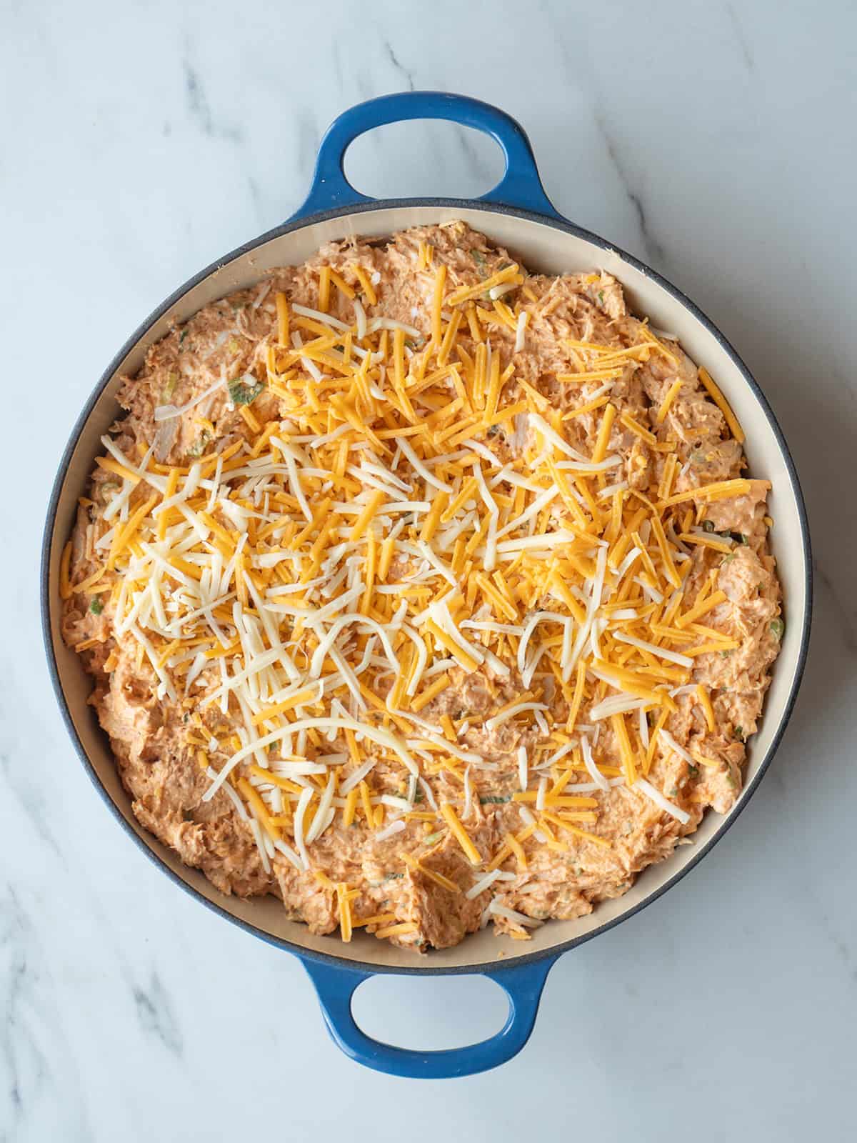 Buffalo chicken dip assembled in a dish before going in the oven