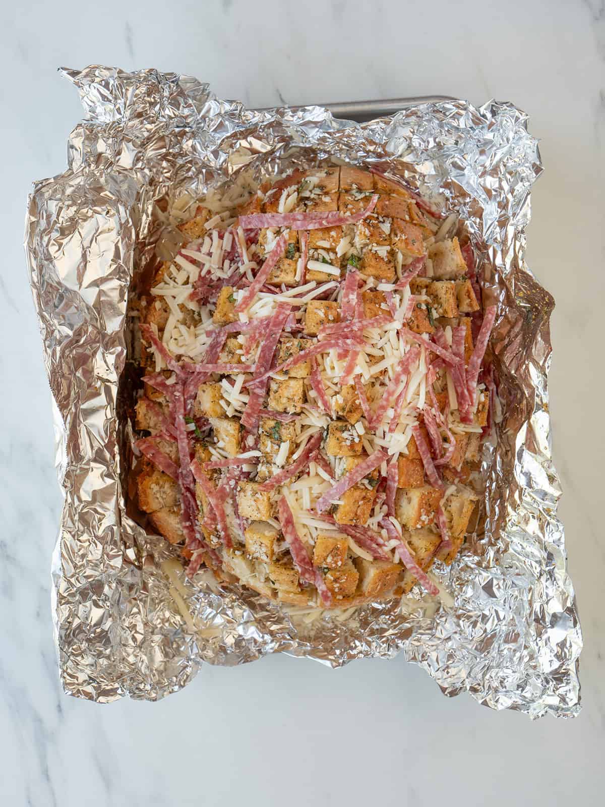 Mozzarella cheese, Pecorino Romano, and Salami in the cuts of the bread for Cheesy Pull-Apart Bread