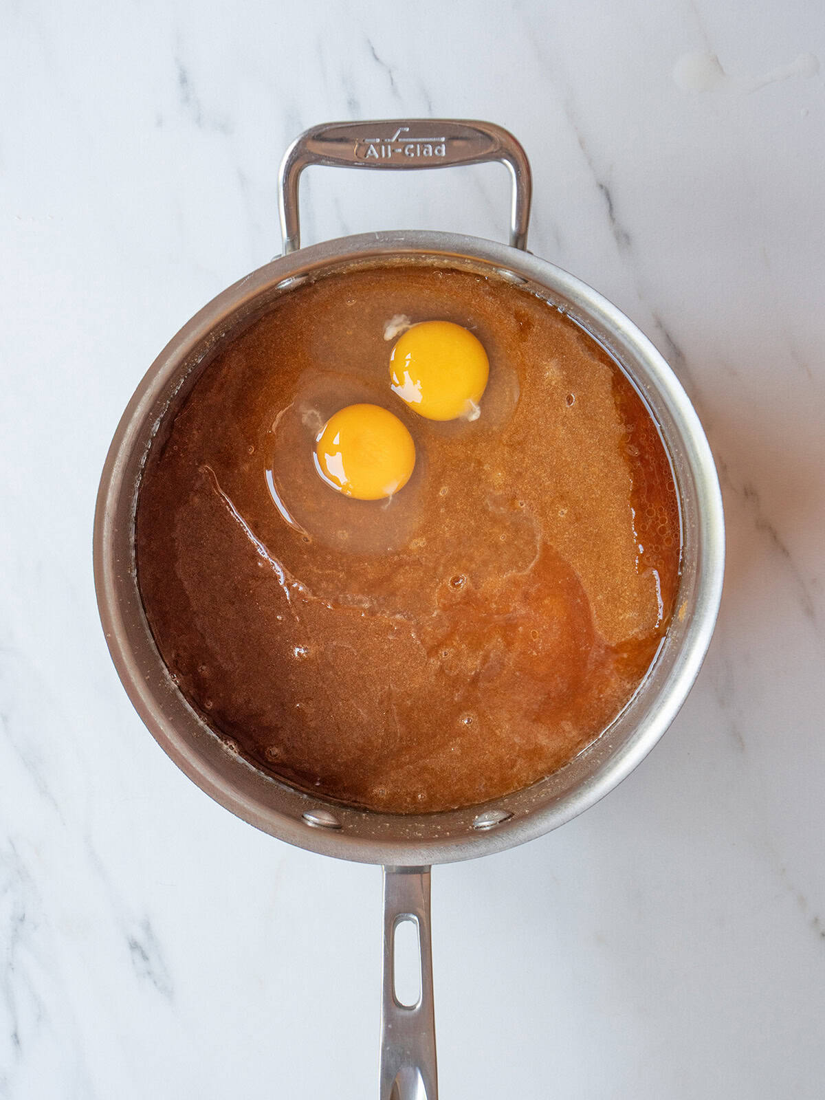 Two eggs added to the melted butter and sugar mixture in a medium pot