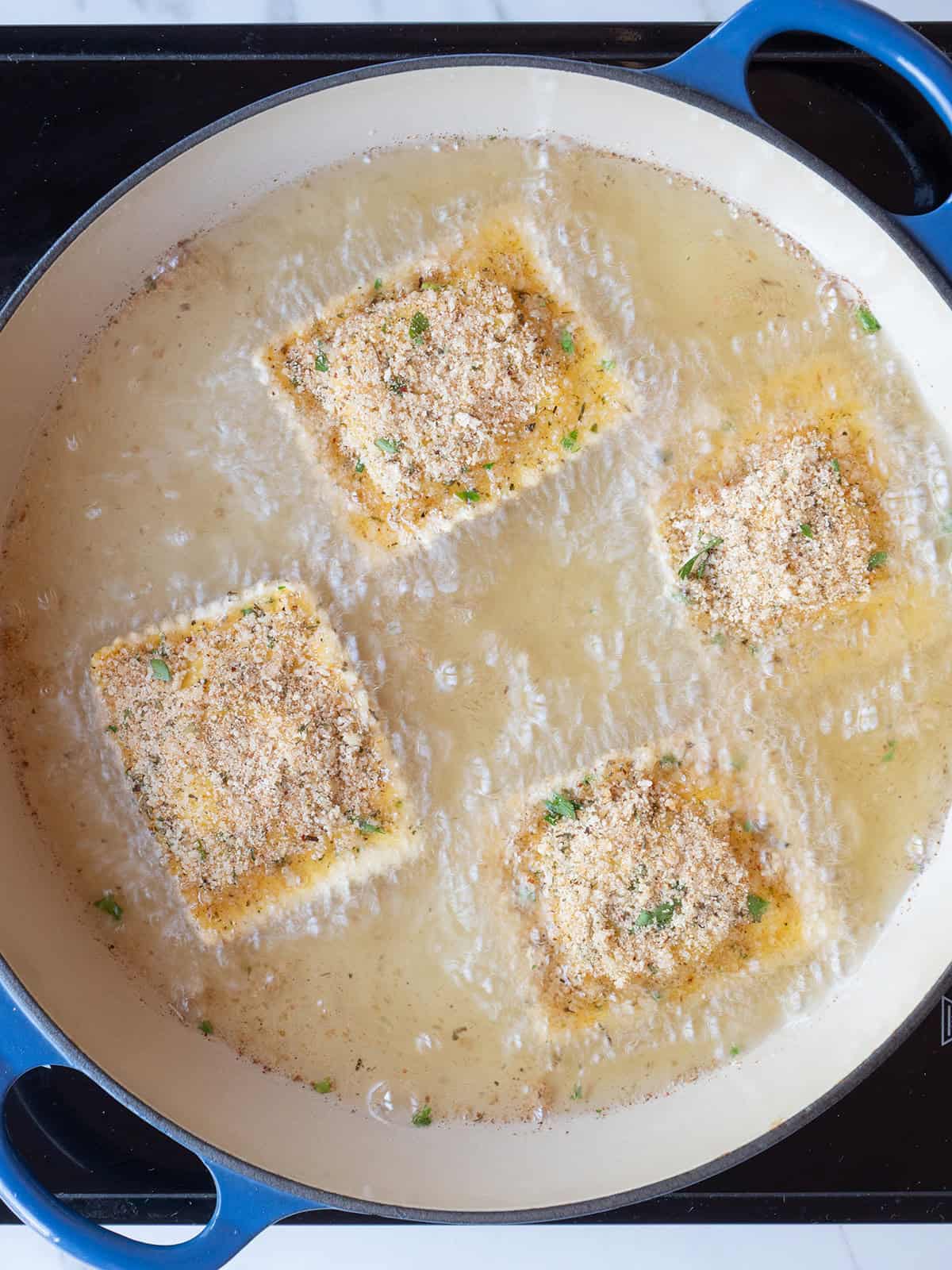 Coated ravioli being fried in a large pan