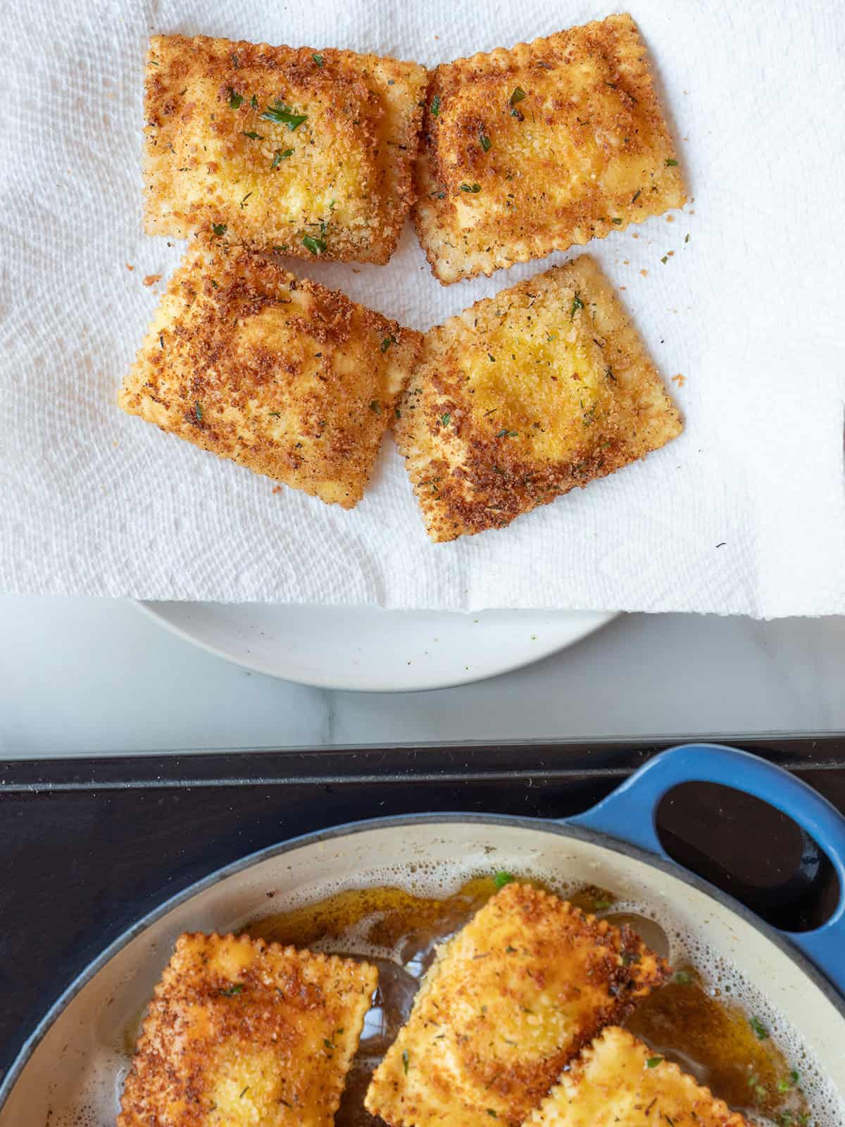 Fried ravioli on a paper towel-lined plate and ravioli being fried