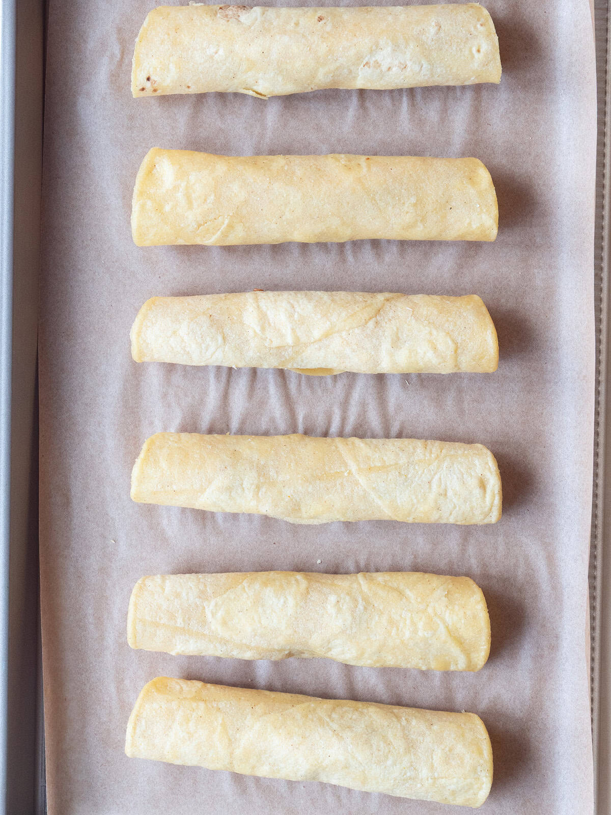 Homemade Chicken Taquitos on a parchment-lined baking sheet prior to frying