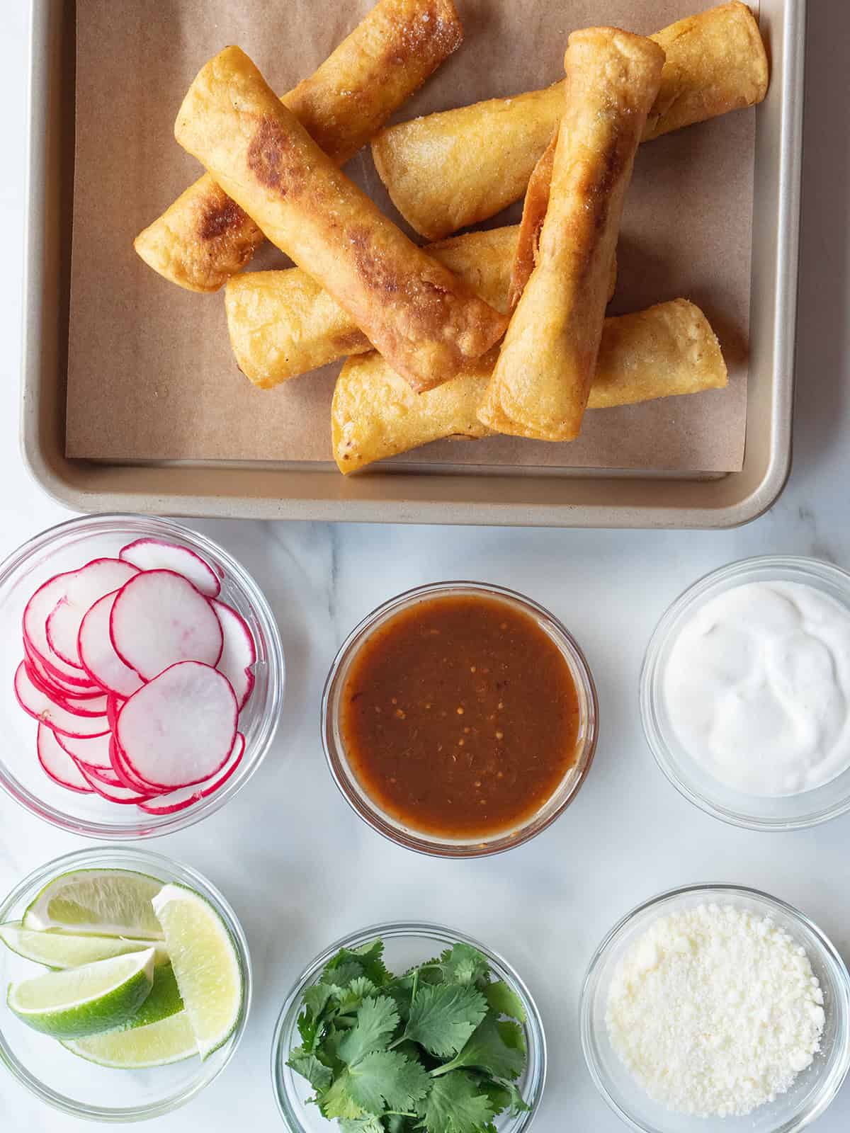 Homemade Chicken Taquitos on a parchment-lined plate with various accompaniments