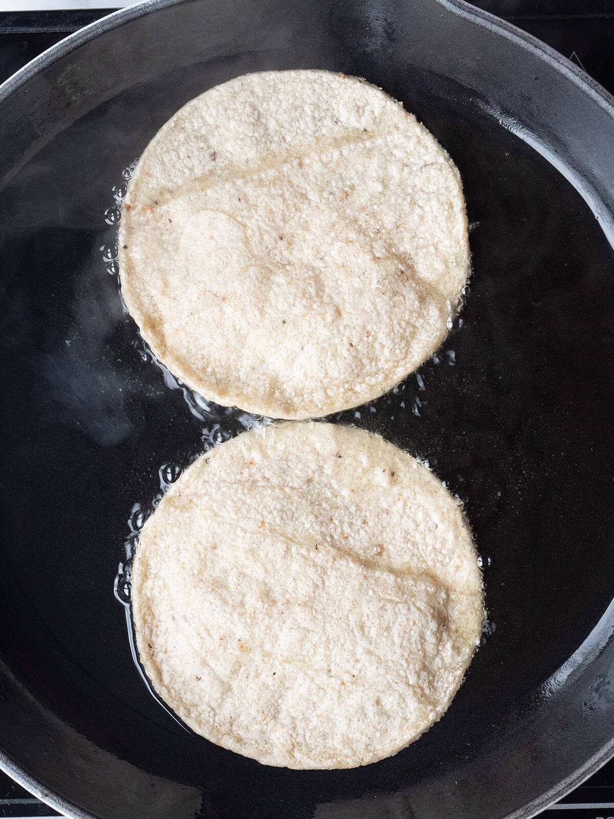 Corn tortillas frying in oil in a skillet for Huevos Rancheros