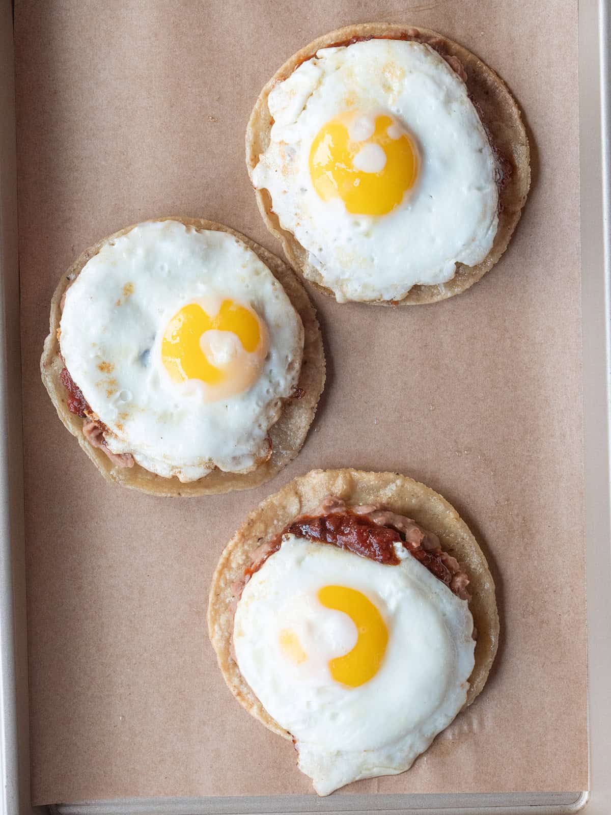 Fried eggs added to the top of Huevos Rancheros on a parchment lined tray