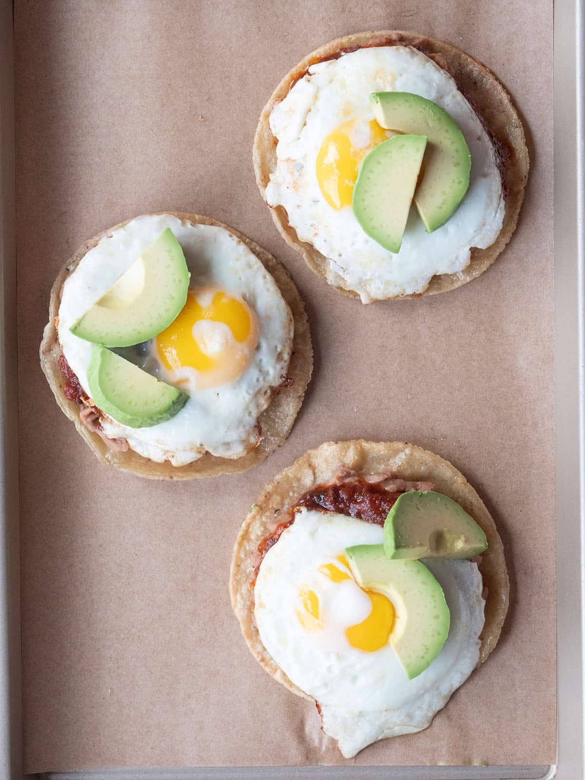 Avocado added to the top of Huevo Rancheros on a parchment lined tray