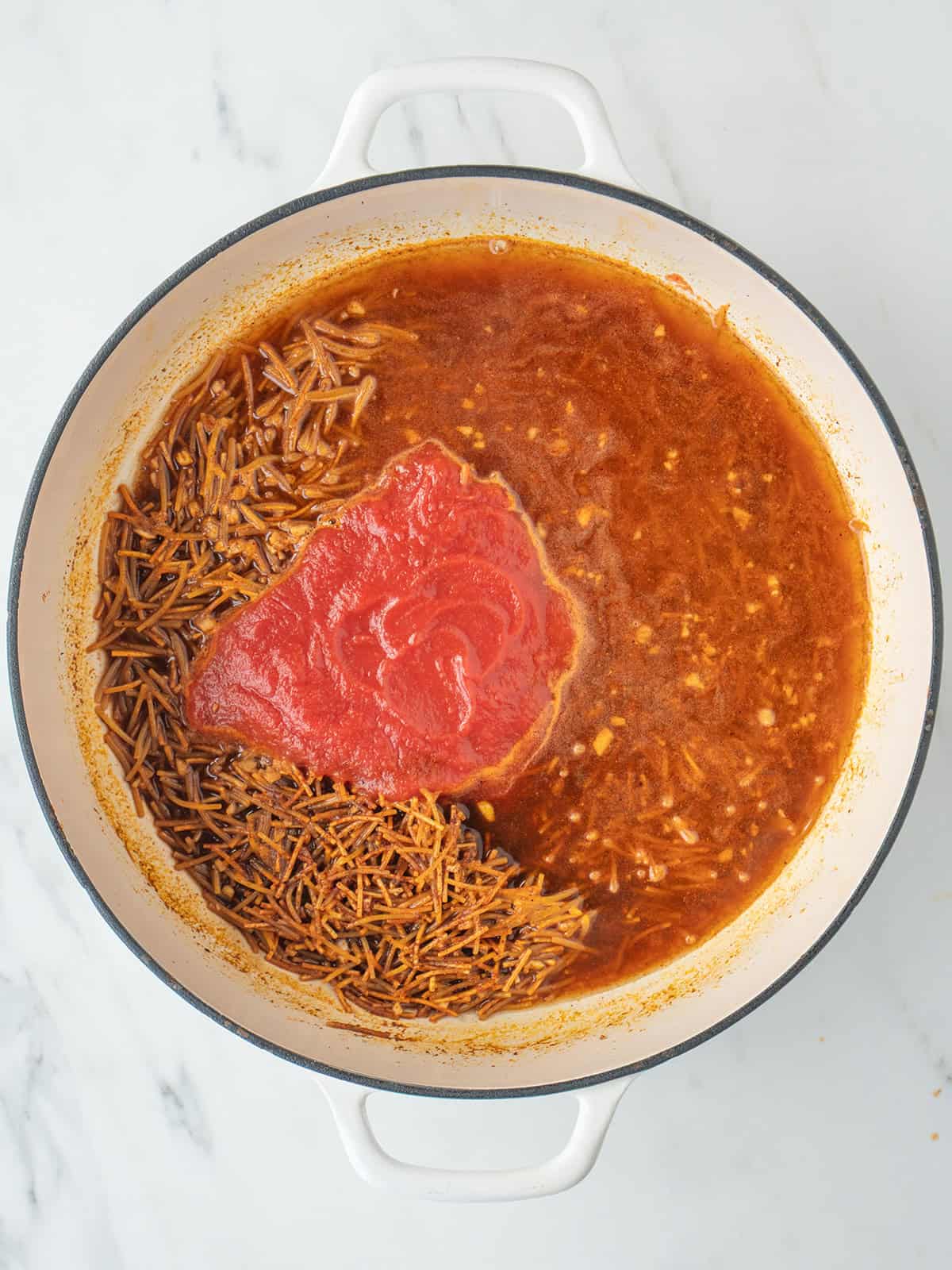 Pasta, broth and tomato sauce in a large dutch oven for Sopa de Fideo