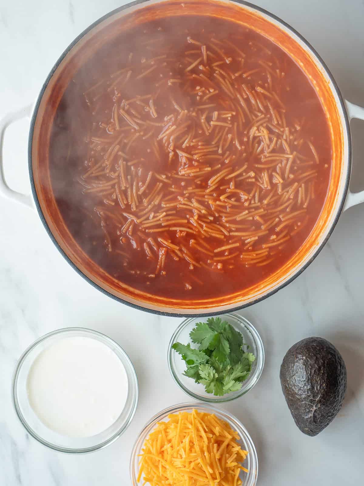 Sopa de Fideo simmering with garnishes on the side in small bowls