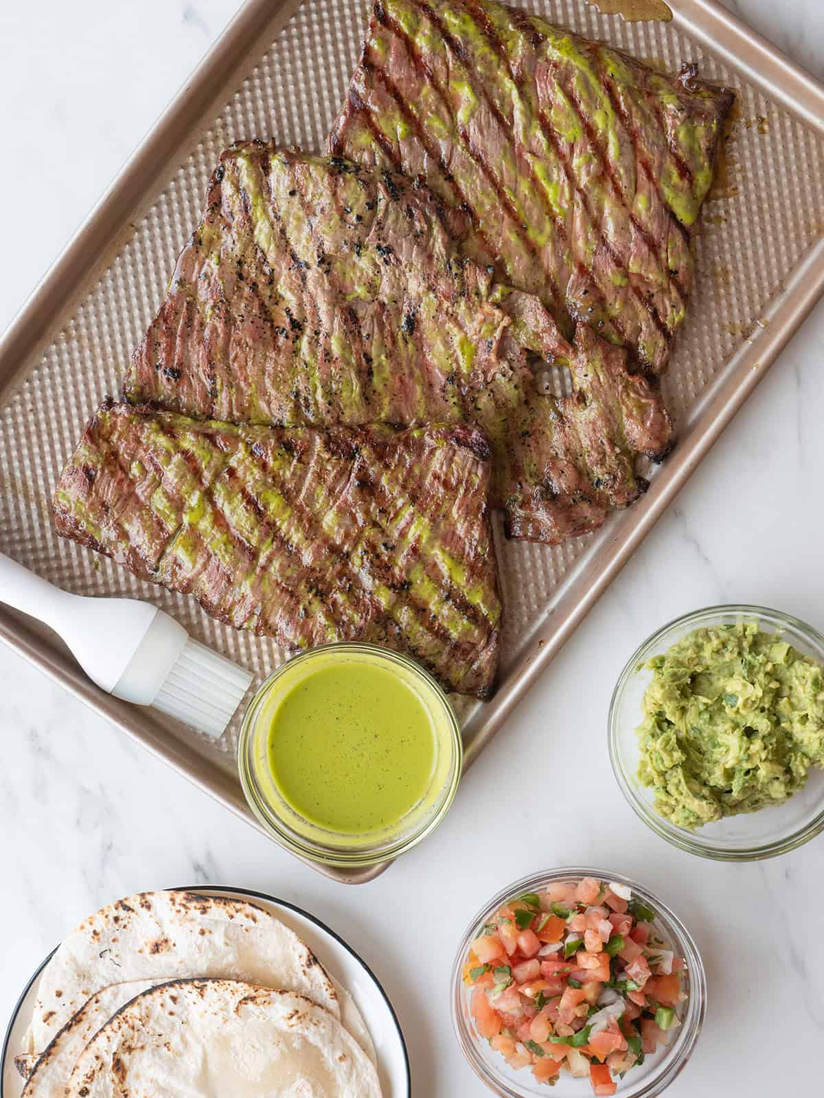 Finished Carne Asada on a tray with sides of guacamole, pico de Gallo, and tortillas