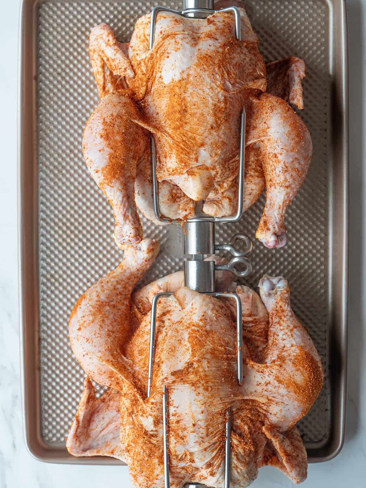 Raw chicken for the perfect rotisserie chicken rubbed with a spice blend on a spit