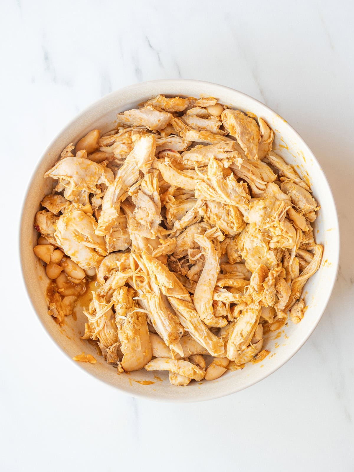 Cooked chicken thighs being shredded before returning to the chili
