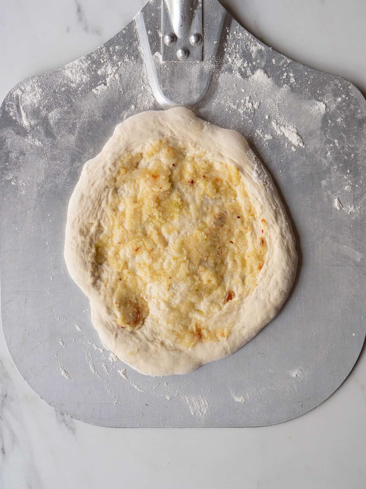 Raw pizza dough topped with garlic paste on a peel