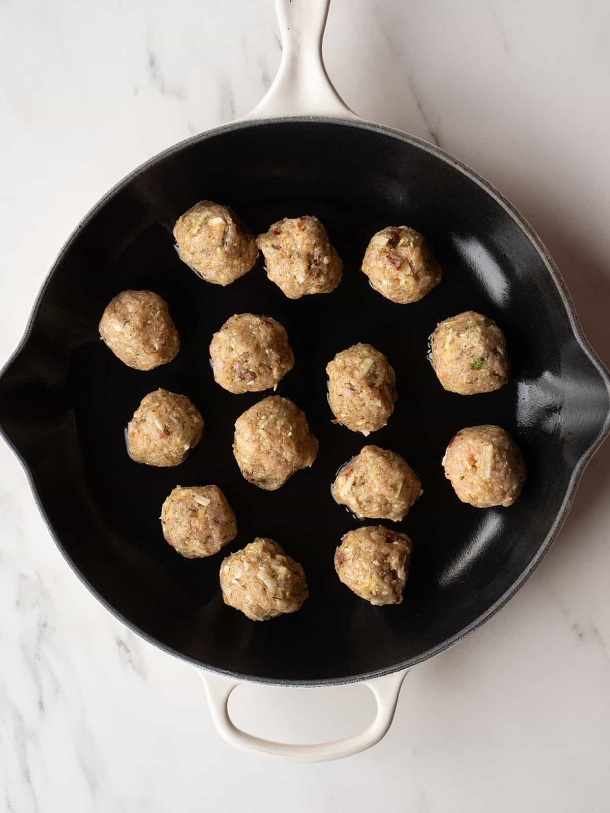 Raw meatballs arranged in skillet