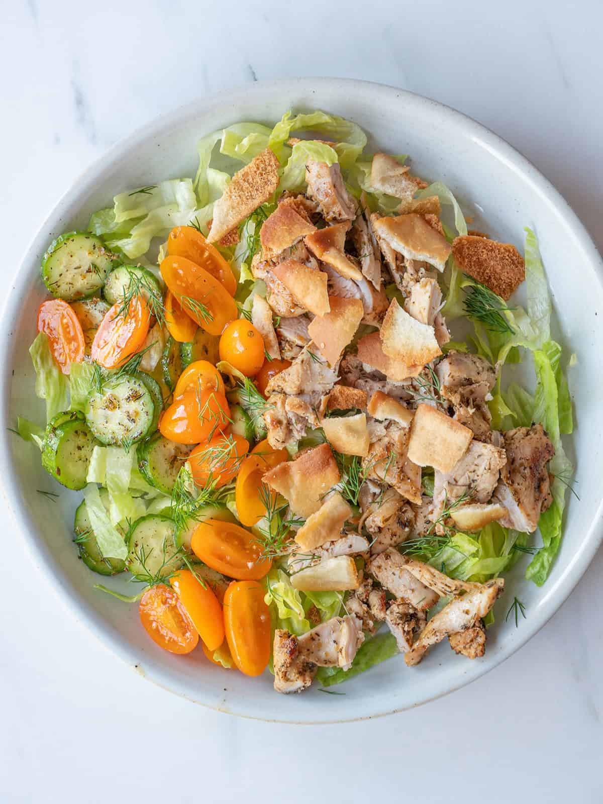 Greek Chicken Bowls with sliced chicken thighs, tomato cucumber salad, romaine, crushed pita chips, and fresh dill