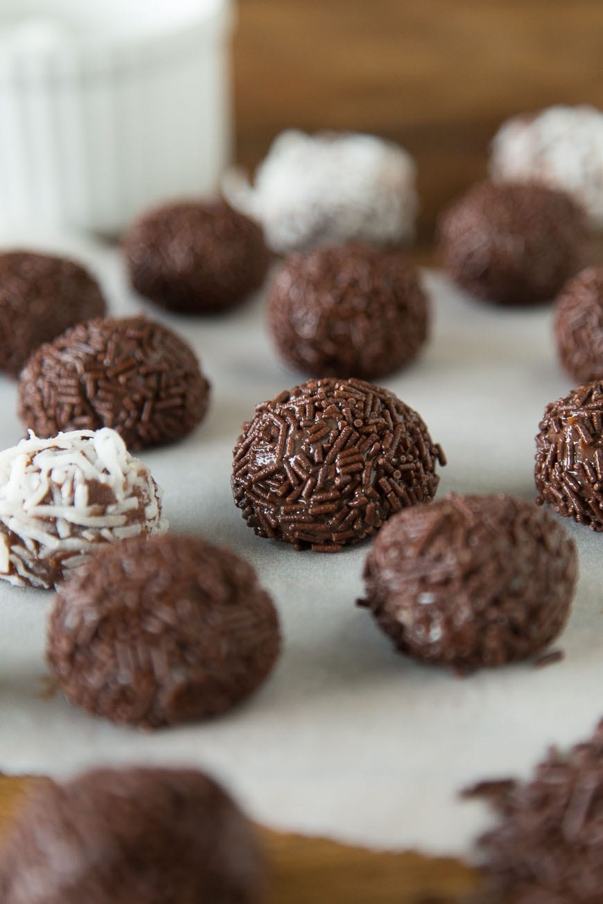 A parchment-lined baking dish with Brigadeiro, some coated in chocolate sprinkles and some in coconut, with the background blurred out.